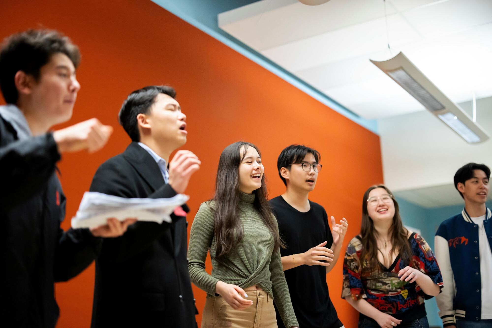Students in the PennYo group singing and practicing in unison. Some have their arms slightly raised as they practice and some of the students are smiling.