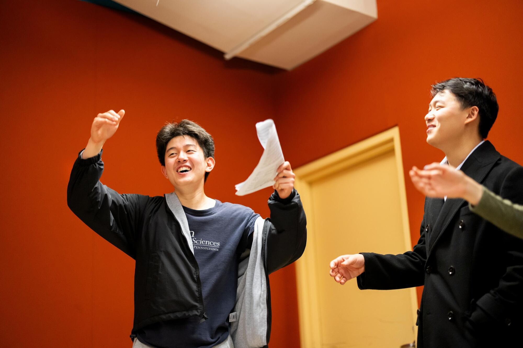 A student in the PennYo group smiling with arms raised while singing. Another student is smiling at him to the right.