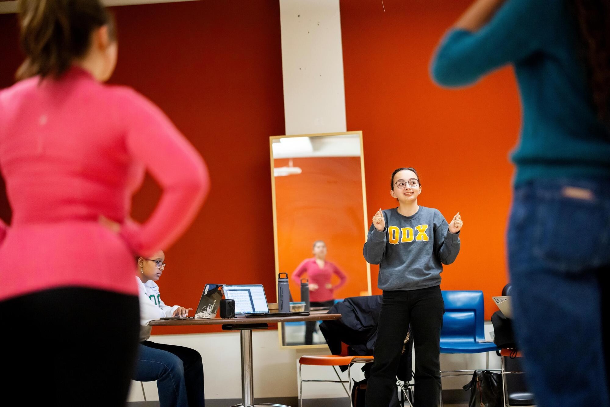 The student-director of Quadramics is providing instruction to the group members. The director's arms are up with fists clenched and they are smiling.