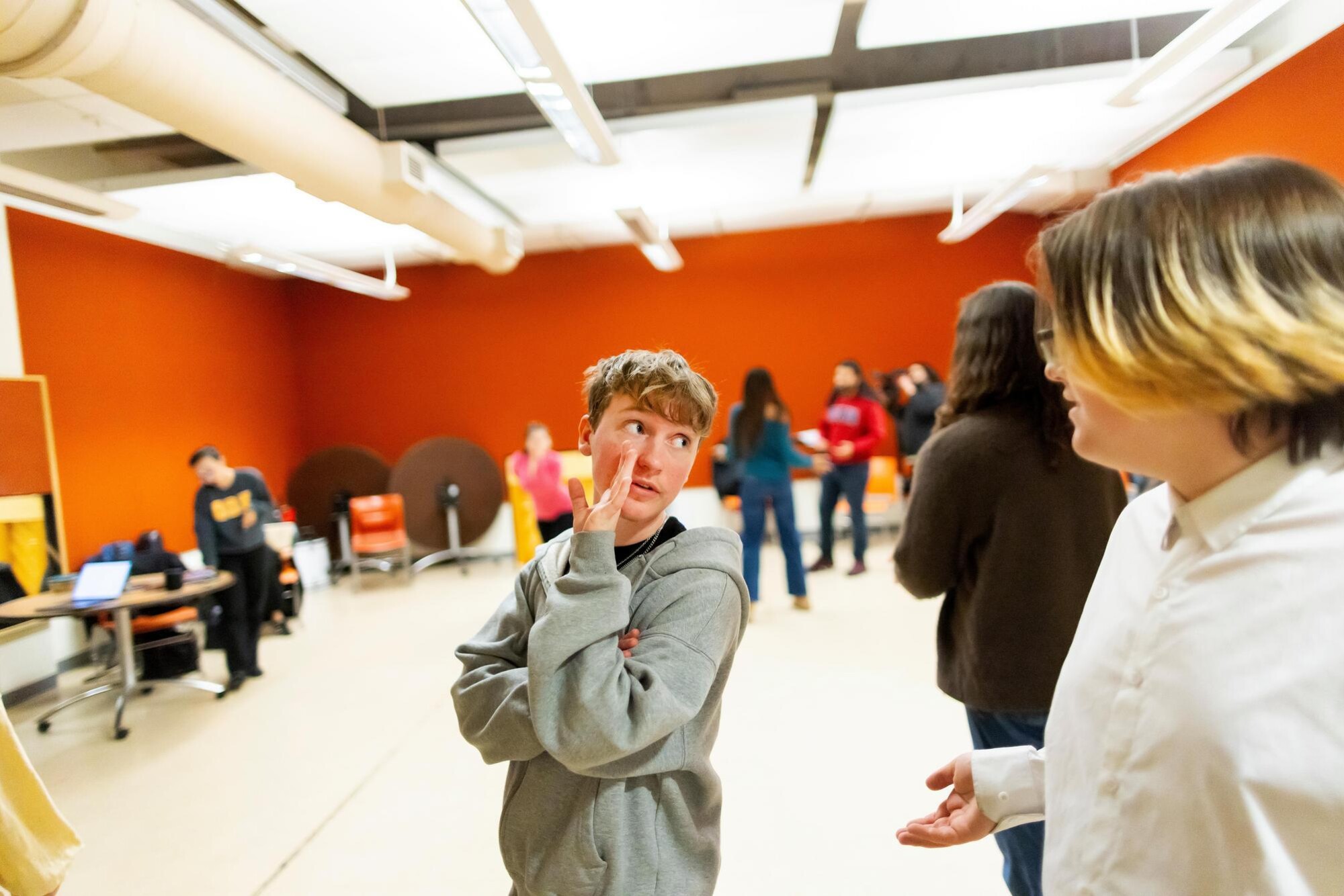 A student in the Quadramics group is pictured striking a pose while speaking with a peer. Fellow group members are practicing in the background.