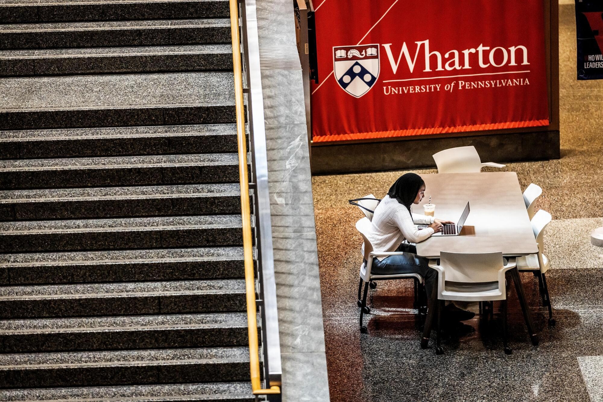 A person working on a laptop near a Wharton sign during Reading Days.