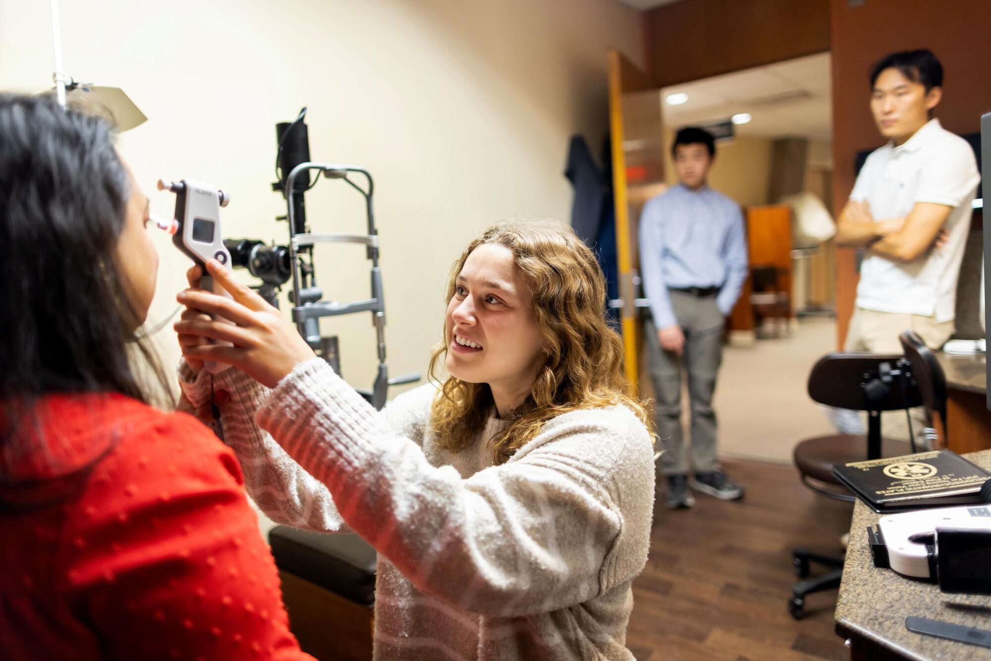 Janine Haros administering an eye screening exam at the Scheie Eye Institute. Fellow team members Eric Lee (center) and Justin Wang (right) are observing in the background.