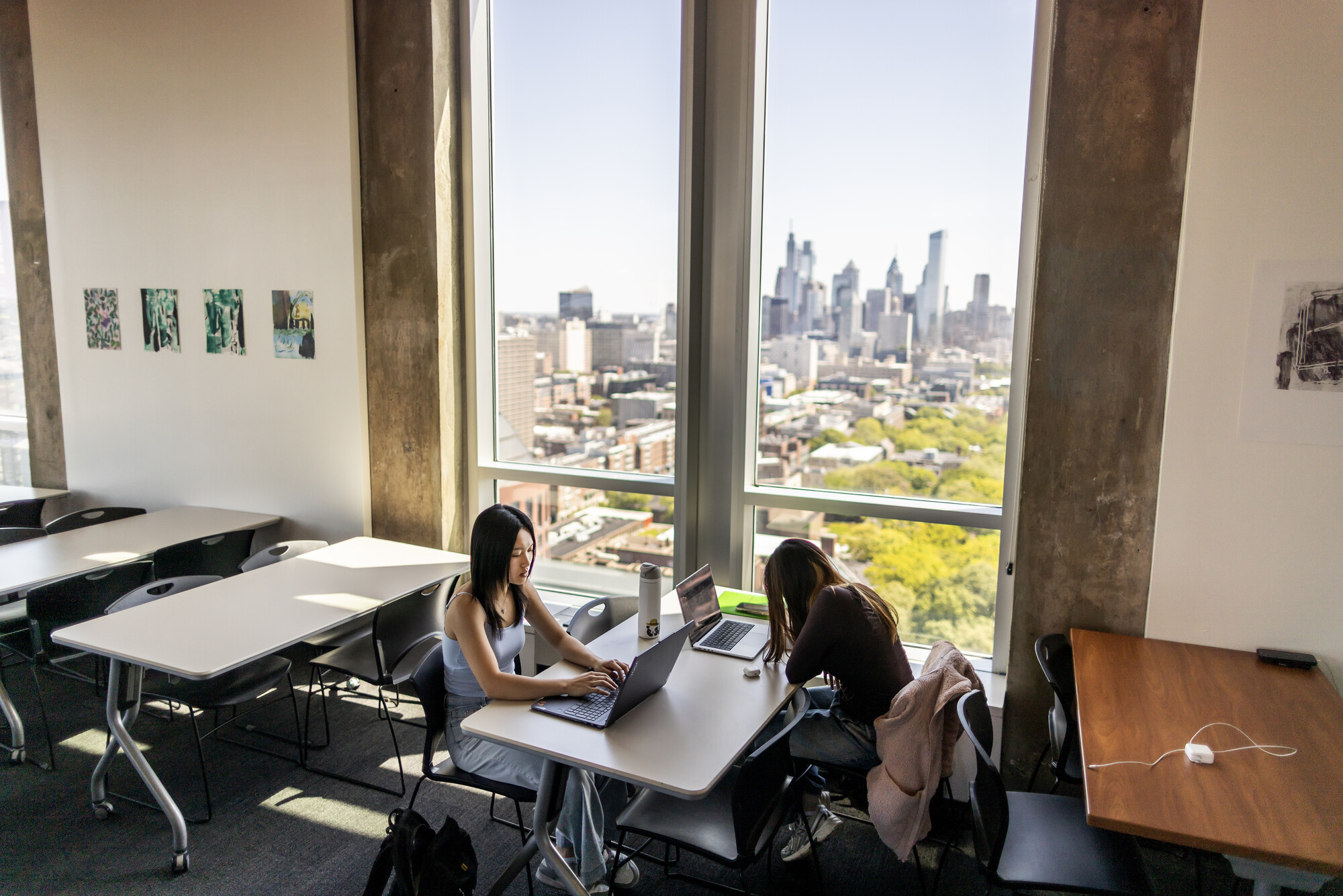 Two students studying at a table with the city of Philadelphia visible through the window.
