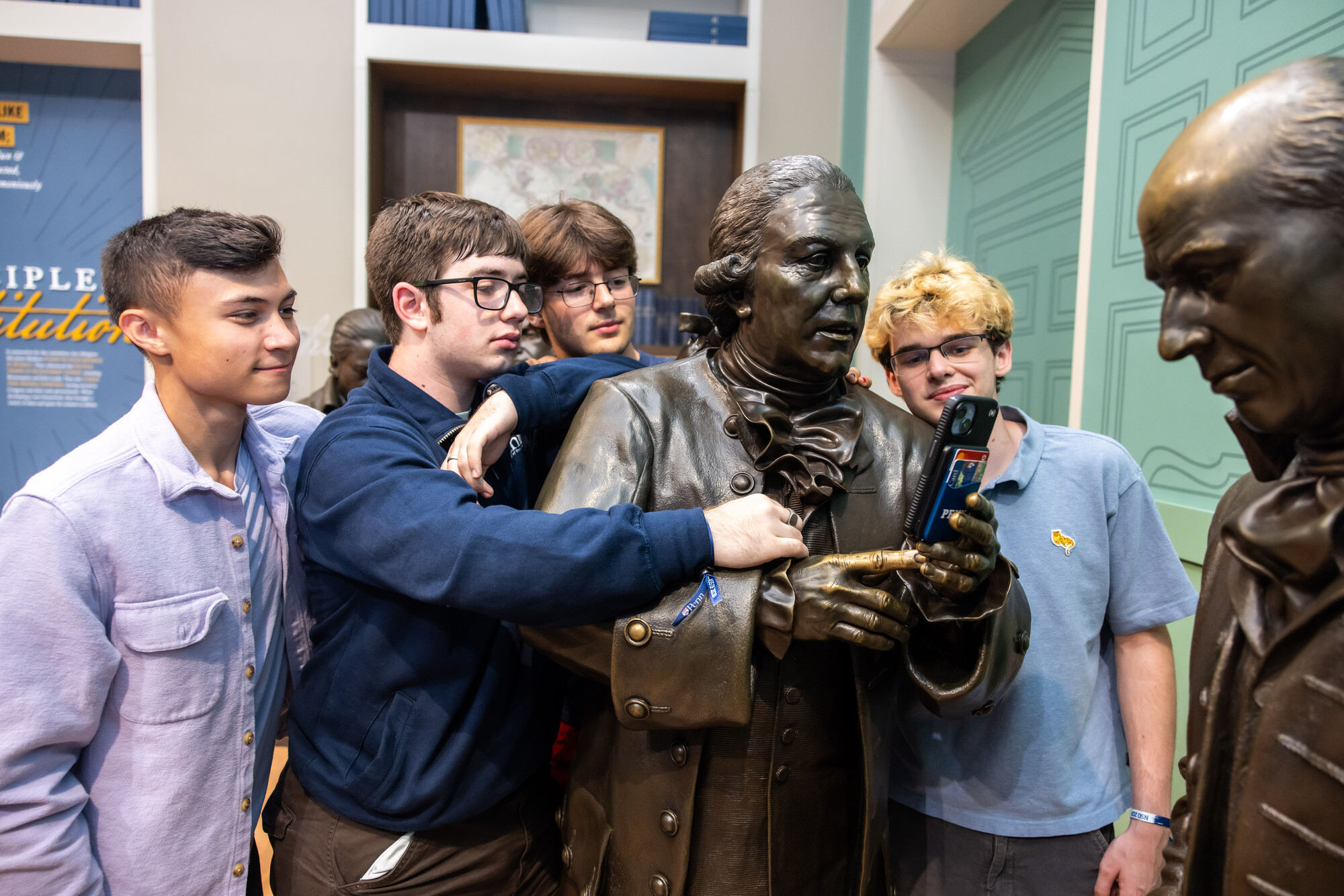 Penn students putting a smartphone in the hands of a statue at the Constitution Center.