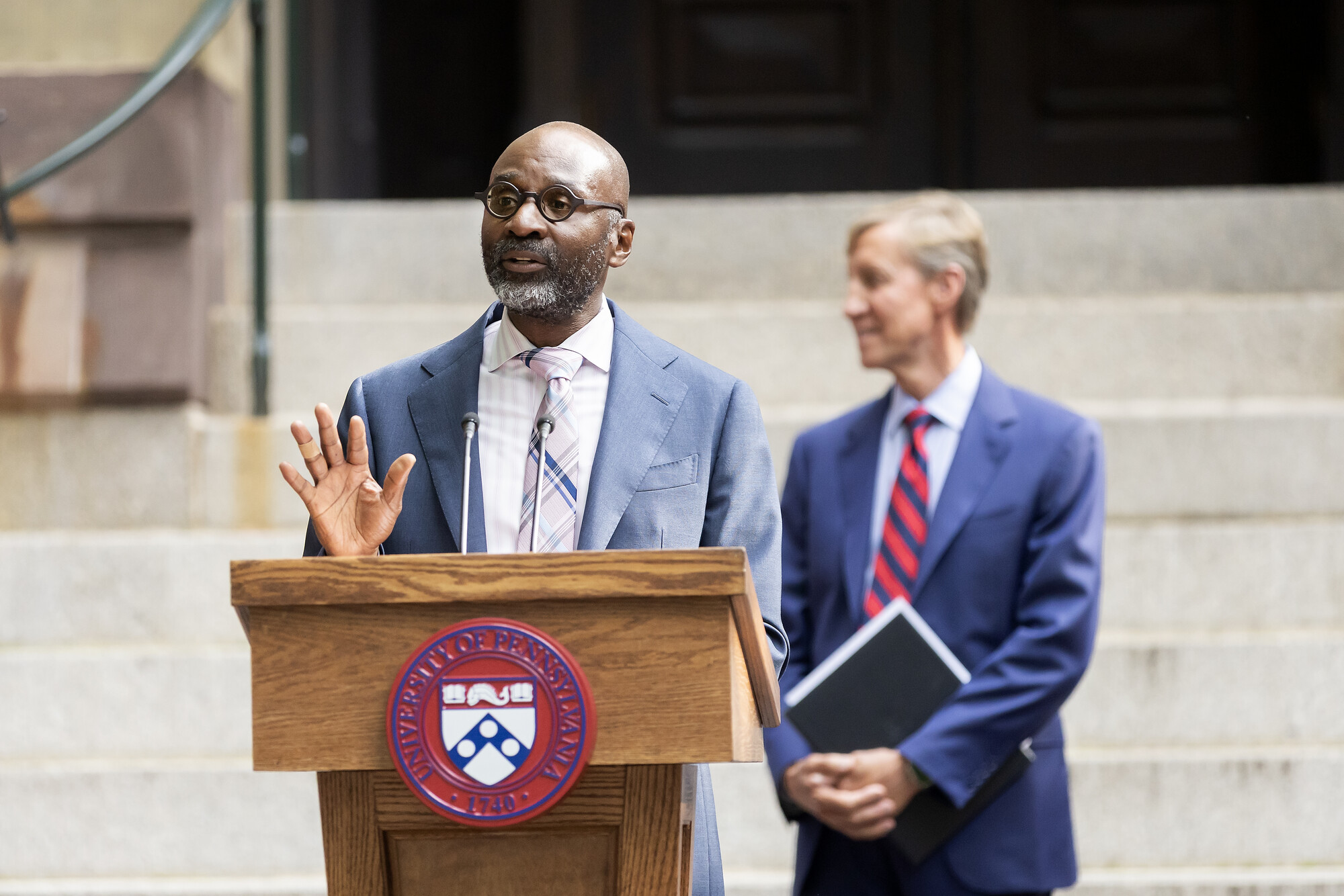 Penn Provost John L. Jackson, Jr. at the podium with J. Larry Jameson behind him in front of college hall.