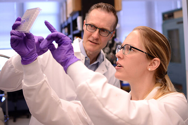 oliver-garden-and-sabina-hlavaty-wearing-latex-gloves-hold-up-a-plate-of-medical-cells-
