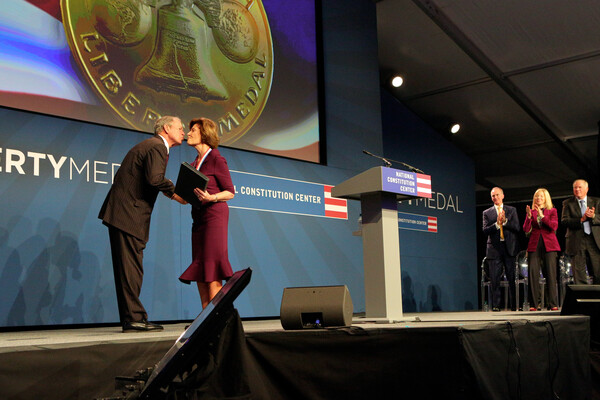 George W. Bush accepting award from Laura Bush on stage with President Gutmann clapping at the far end of the stage