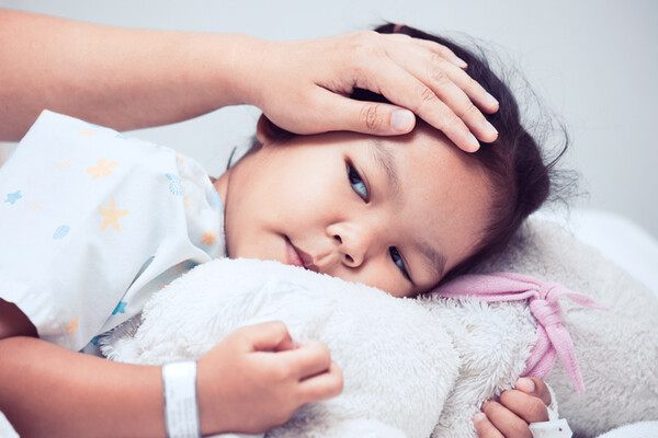 sick child in bed with adult hand on forehead