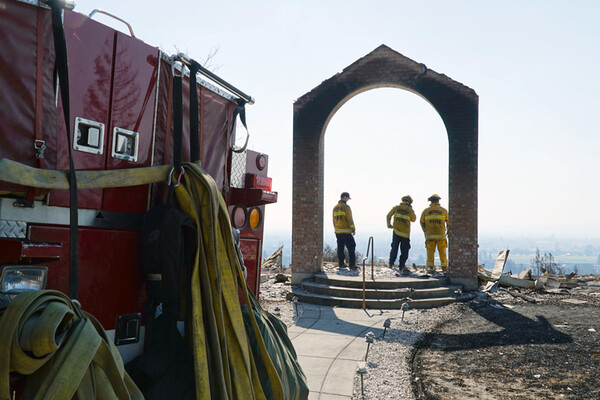 firefighters in remaining archway of a destroyed building with side of firetruck in foreground