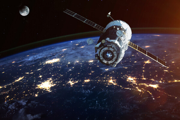 a satellite flying above earth with the moon in the distant background