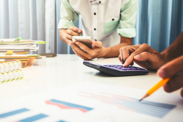 two people at a desk with calculators, papers, pens and pencils
