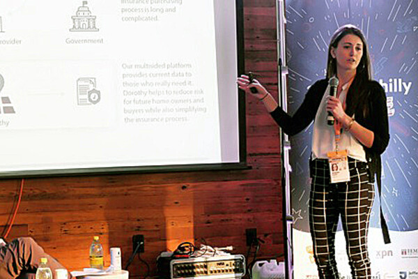 Arianna Armelli standing and addressing room pointing to a screen and holding a microphone