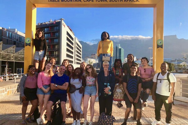 Group of students and professor gathered at monument with mountain in back.
