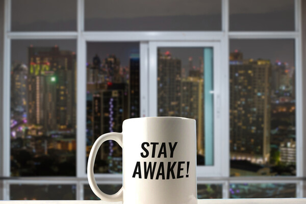 mug on windowsill overlooking the city at night that reads Stay Awake!