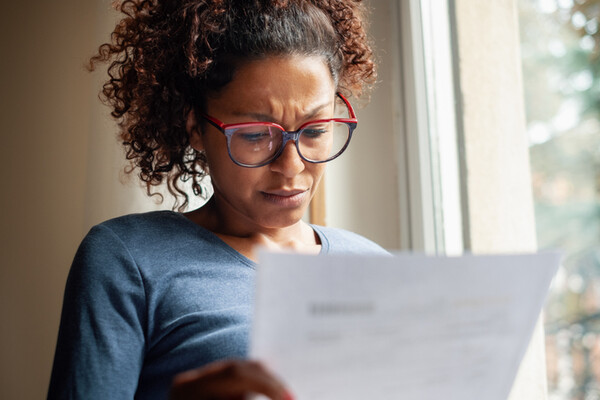 person wearing glasses holding a piece of paper and frowning