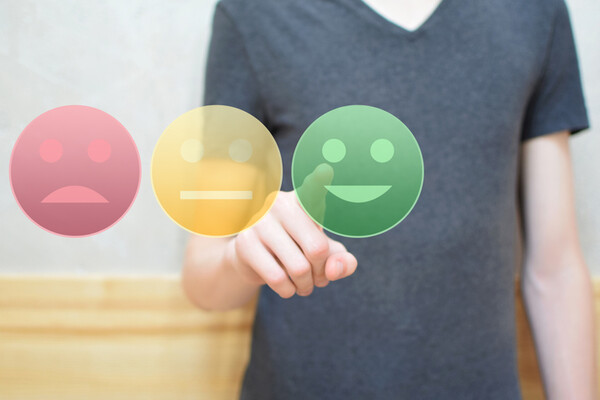Person pressing one of three large digital buttons with a happy, neutral, and frown face.