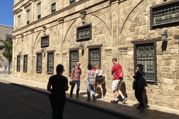 A group of people walking in front of a stone building in Haifa, Israel.