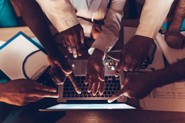 many hands in pointing to a computer, one holding a stethoscope, indicating doctors