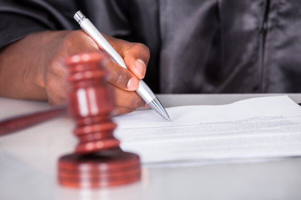 judge's hand writing with a pen on paper with a gavel in foreground