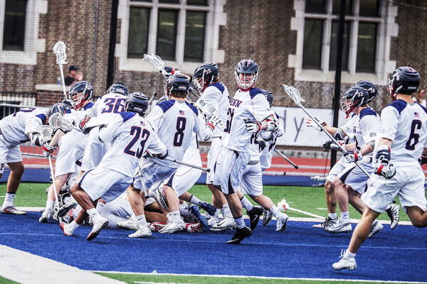 Members of the men's lacrosse team celebrate in a group.