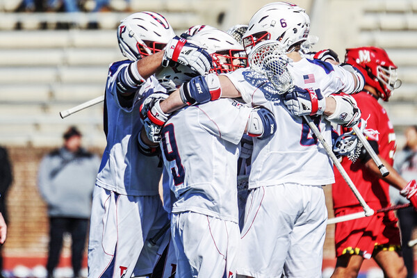 Penn men's lacrosse players celebrate in a circle.