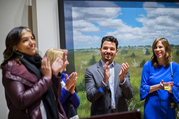 Four people standing in front of a painting, clapping and looking at each other. 