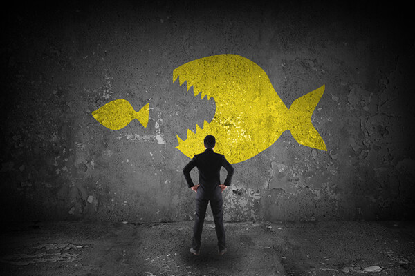Person facing a wall with an drawing of a big fish eating a smaller fish.