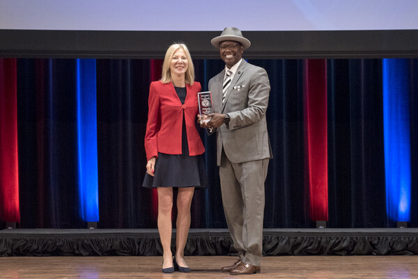 Amy Gutmann and Lorenzo Jackson on stage, Jackson holds an award.
