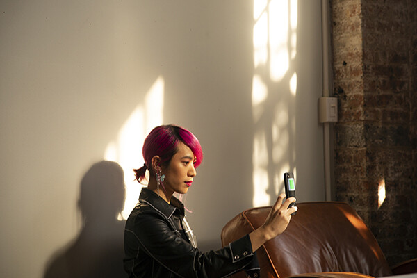 teen holding up a phone inside in the sunglight.