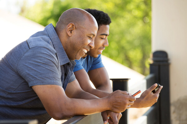 Two people, one older, one younger sitting and looking at their phones. 