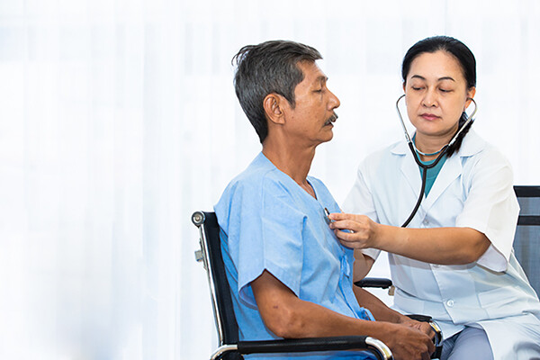 Prostate cancer patient sits in wheelchair while nurse listens to chest with a stethoscope.