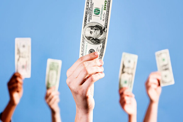 Five hands holding $100 dollar bills in their hands against a blue sky