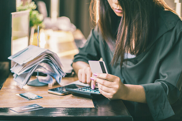 person sits at a table with a stack of bills, three credit cards, computing on a calculator with a cell phone beside it.