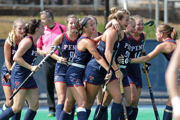 Players on the field hockey team celebrate in a circle on the field.