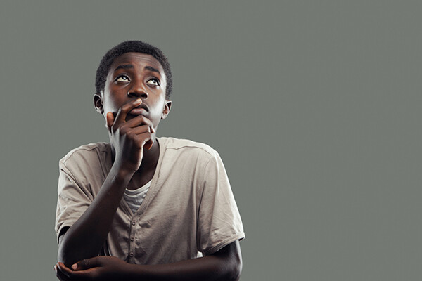 A young student of color looks upward with their hand on their mouth