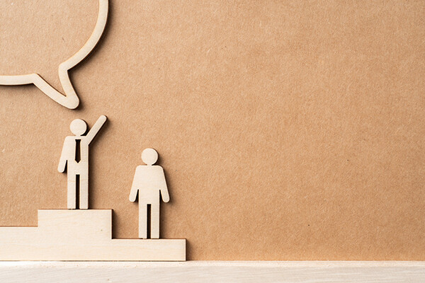 stick figure rendering of a man on a soap box with a dialogue box, a person one step below staying silent.