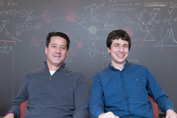michael kearns and aaron roth sitting at a table in front of a chalk board