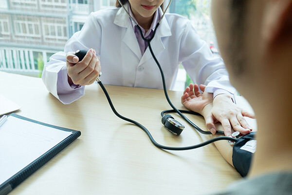 Doctore checks someone's blood pressure in an office with windows and city in background