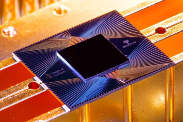 a computer chip with sycamore written on one side, on the top is a pattern of lines that form triangles and the chip is resting on a metal background with orange lighting