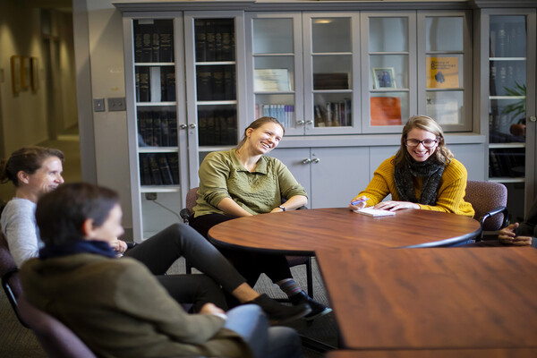 Five faculty members and graduate students seated around tables, talking and laughing