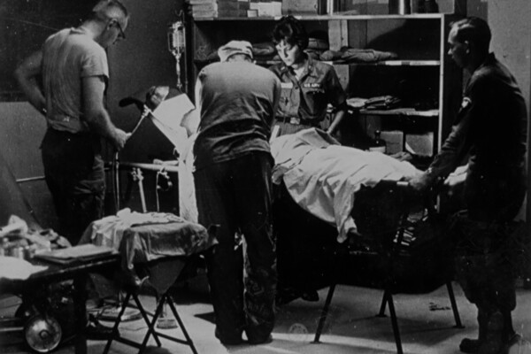 A black-and-white image of health care professionals standing around a patient in a surgical suite during the Vietnam War. 