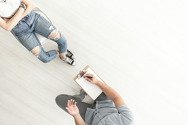 overhead view of a rehab patient with arms crossed and a counselor with a clipboard