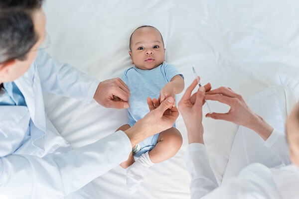 Infant lying on their back with a doctor and nurse standing above with a vaccine injection