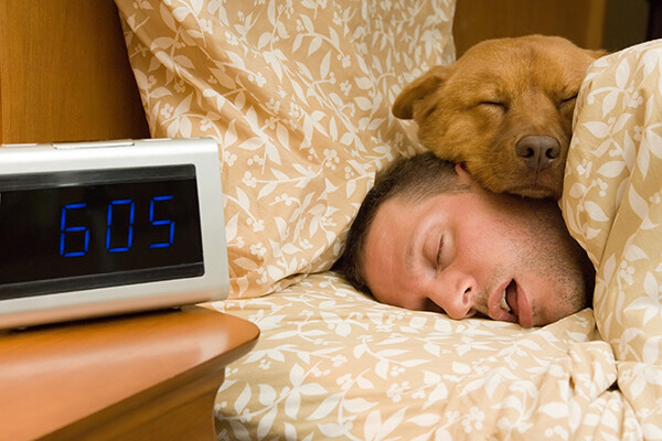 person laying in bed asleep with mouth open, their dog is laying on top of them
