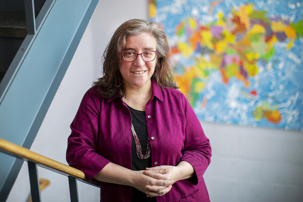 woman with clasped hands stands in a stairwell with colorful art in the background