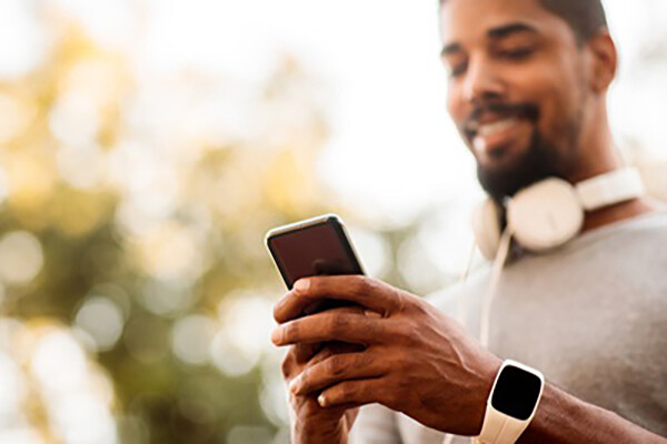 person outside wearing a fitness tracker and headphones looking at a smartphone