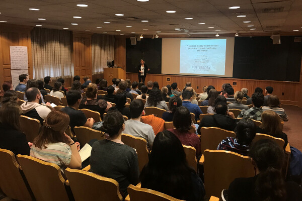 an audience in a lecture hall watching a speaker give a powerpoint presentation