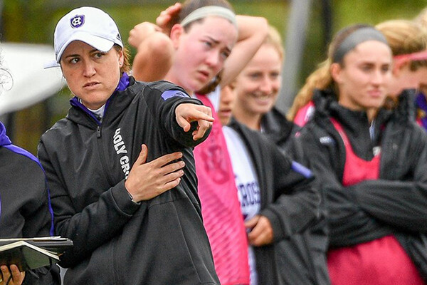 Casey Brown on far left points towards the field while members of the soccer team stand beside her on the sidelines