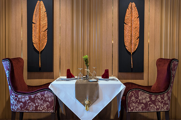 Fancy table setting with velvet chairs, white tablecloth, and gilded leaf wall hangings