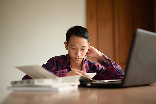 Teenager at a table at home with an open laptop and books.